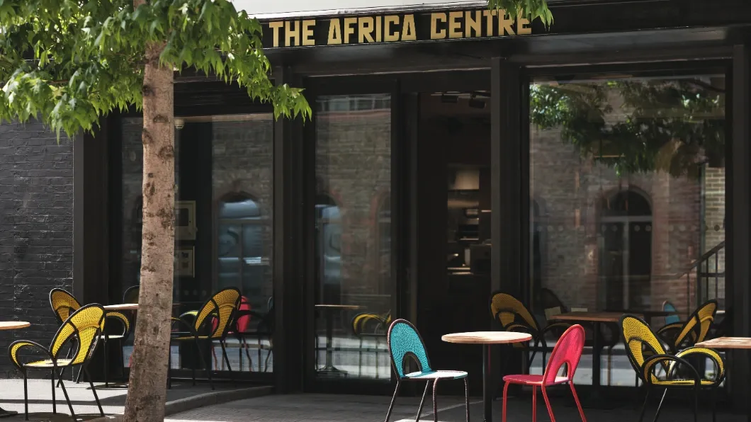 Exterior facade of The Africa Centre with outdoor seating tables and colourful chairs.