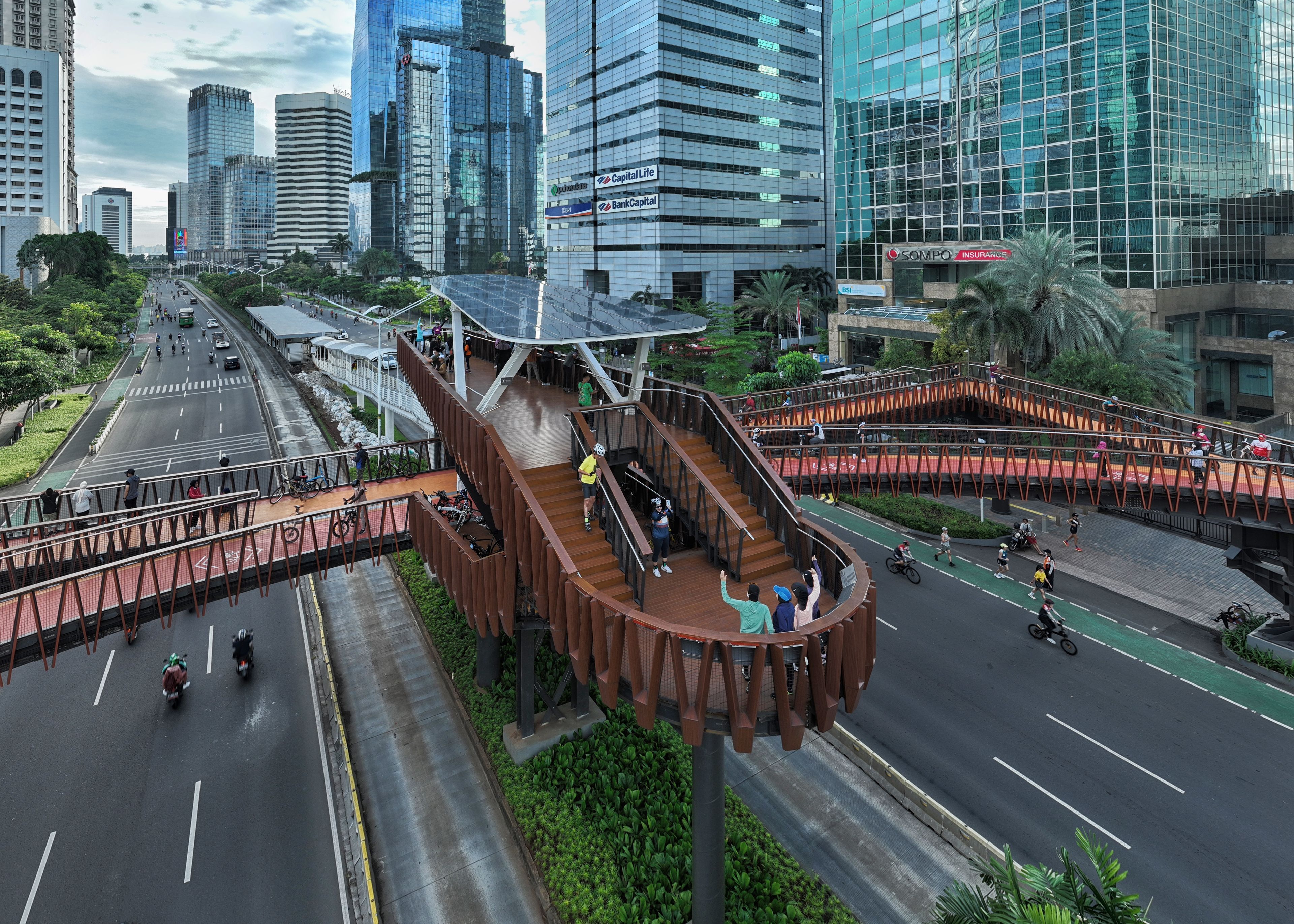 The Pinisi Crossing Bridge in daylight above the city traffic and high-rise buildings in the background.