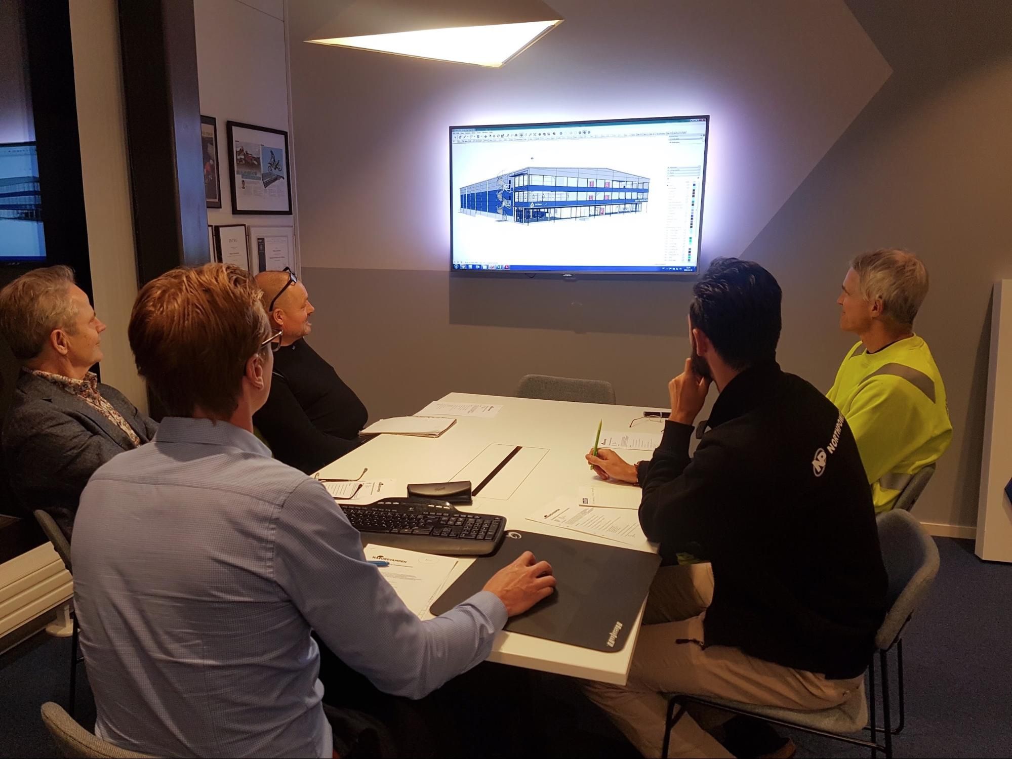 Team meeting in a modern office, reviewing a building design on a large screen.