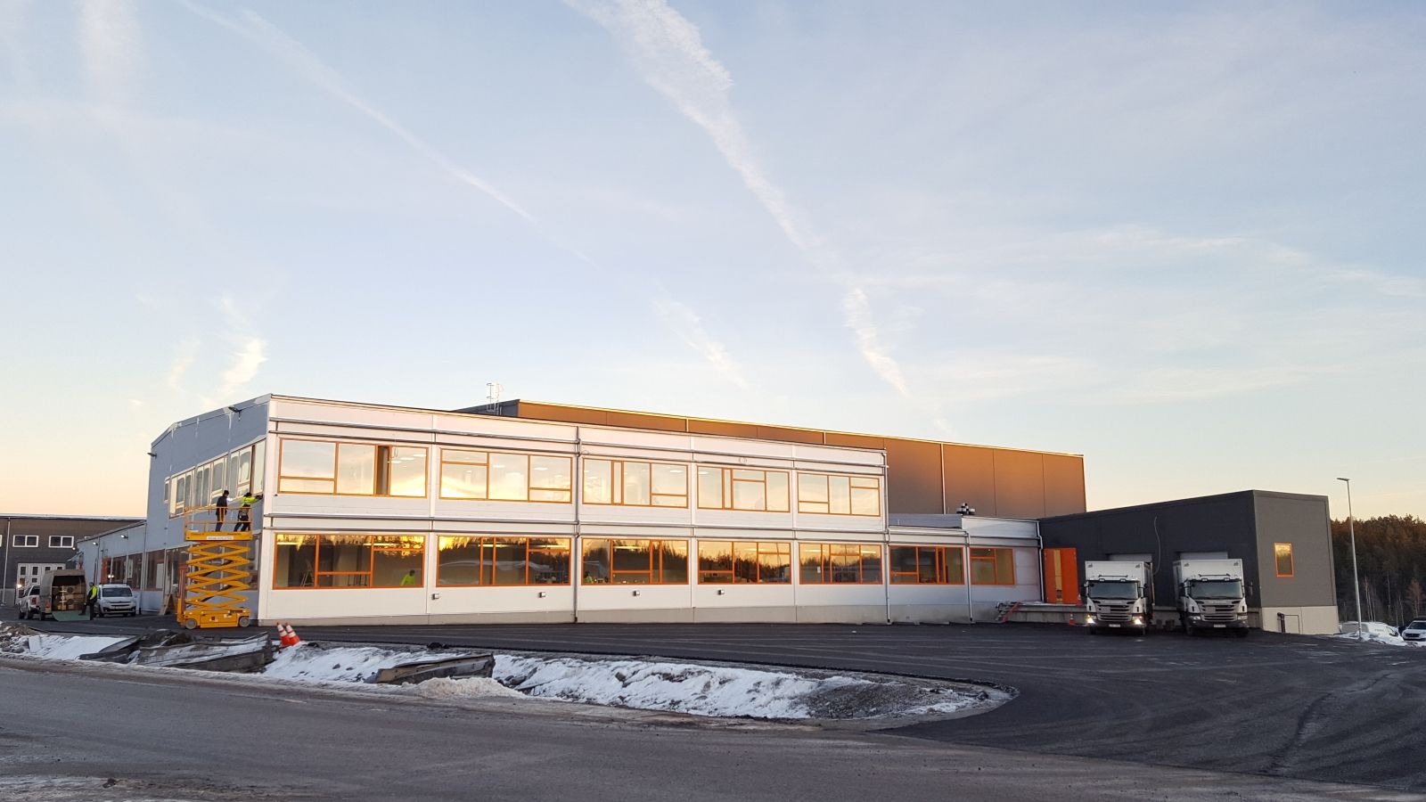 Modern warehouse with trucks parked in front under a clear sky.