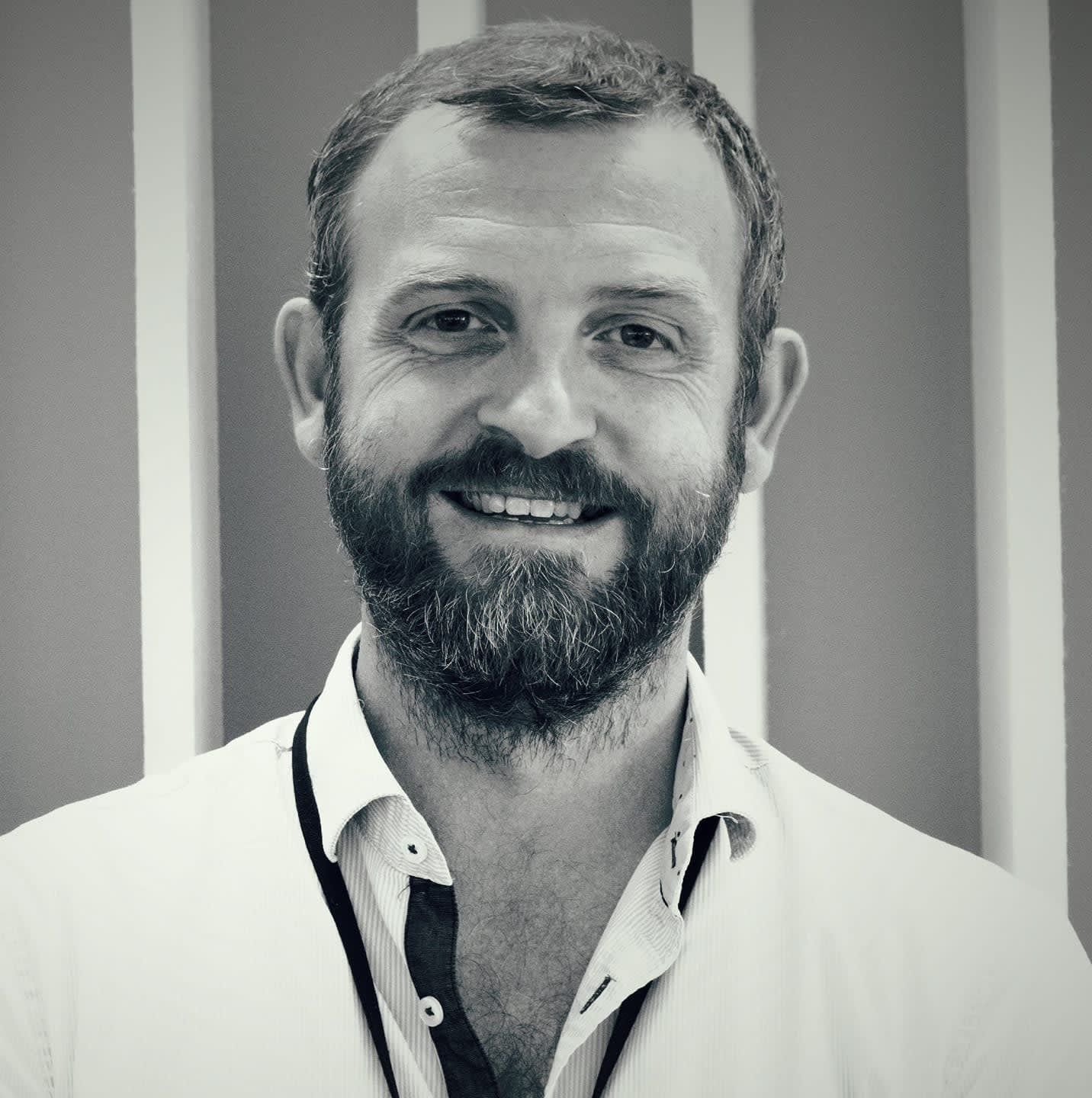Portrait of a smiling man with a beard, wearing a white collared shirt.