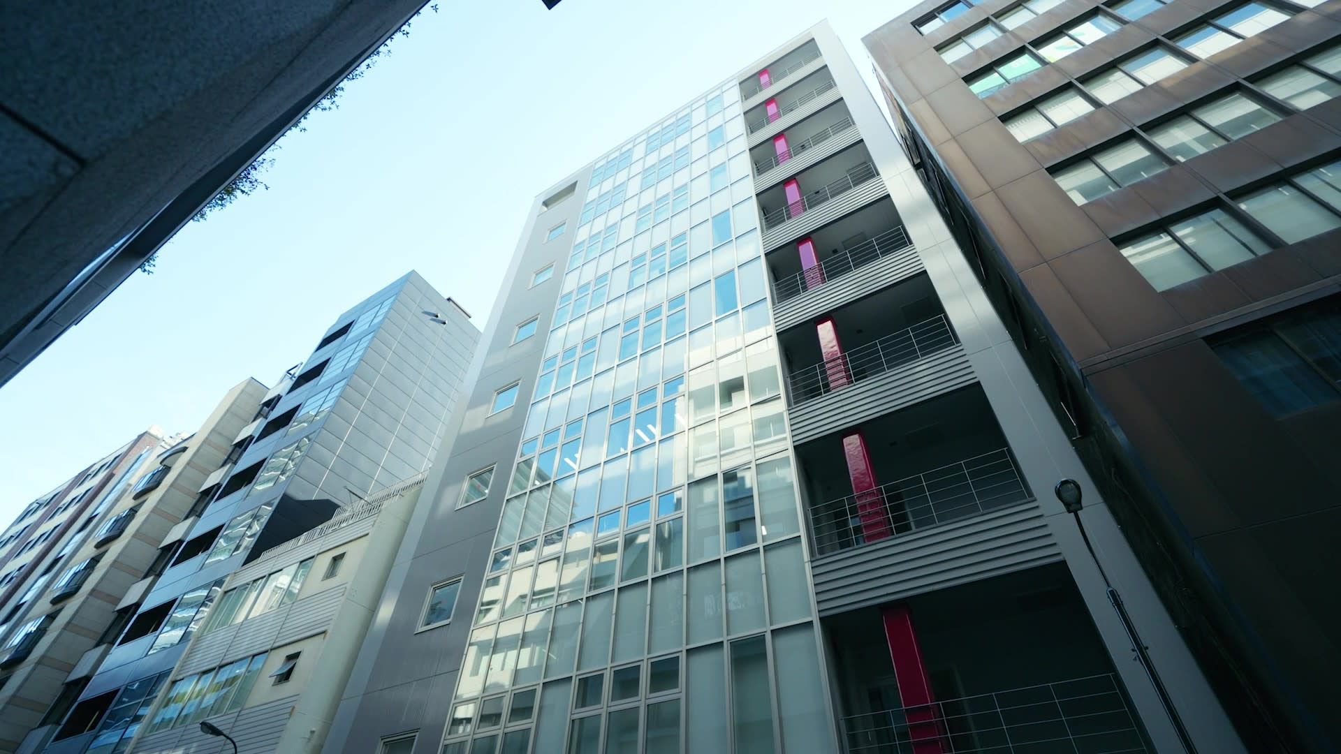 Looking up at a row of modern office buildings with glass facades against a clear blue sky.