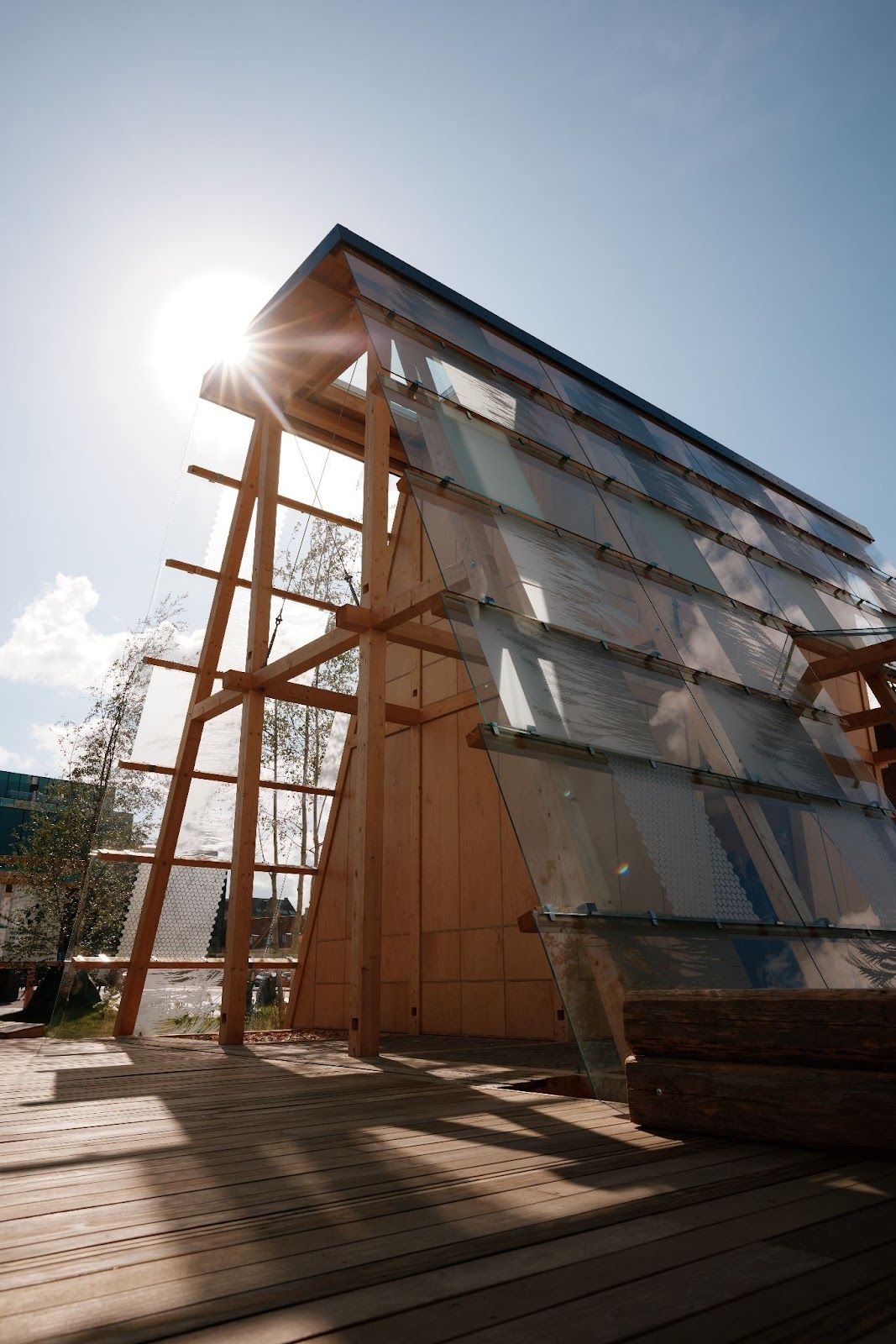 The sun shines on a unique wooden structure with a slanted roof made of transparent panels.