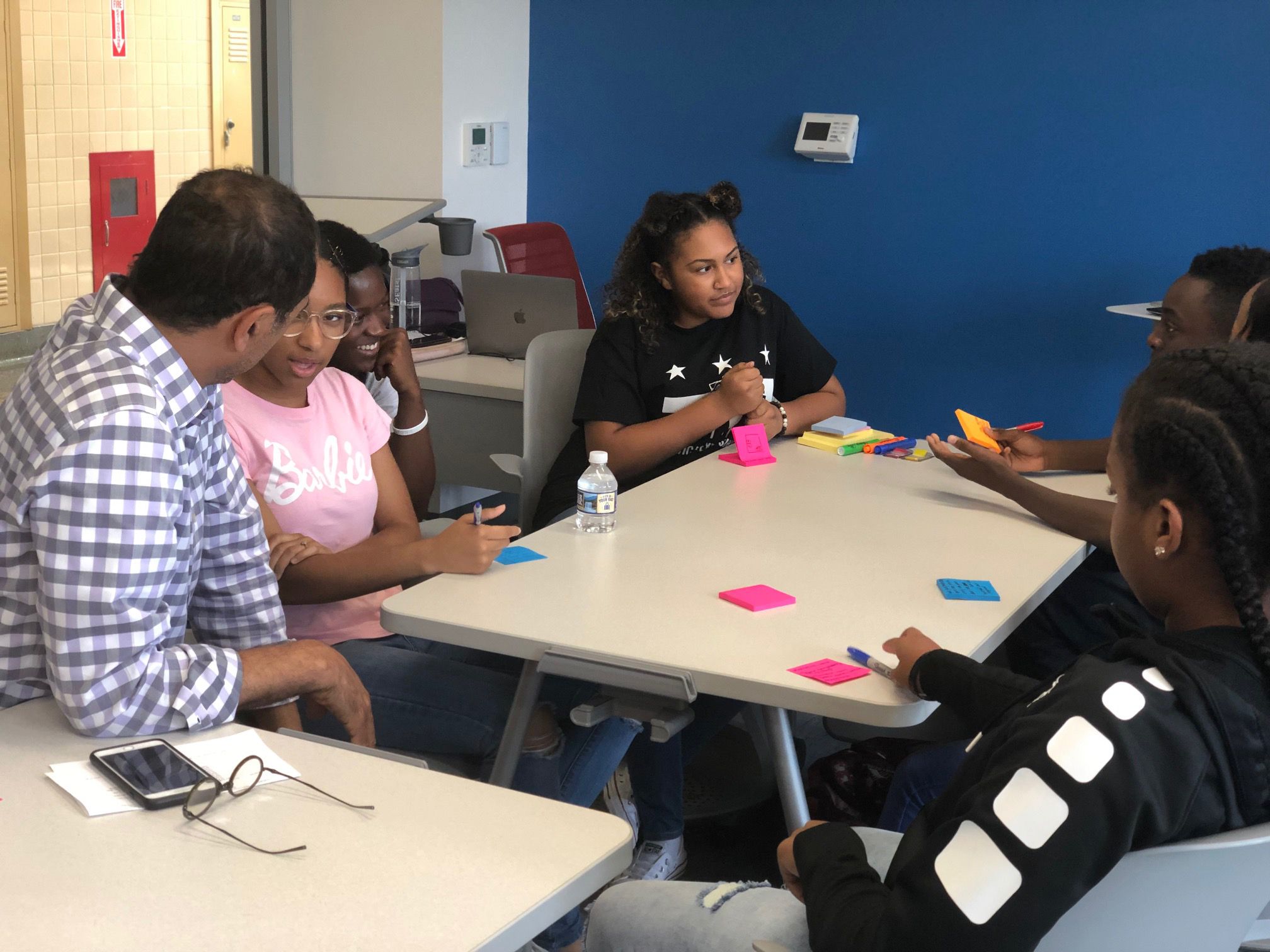 A diverse group of students and an instructor engage in a collaborative session, using sticky notes at a table.