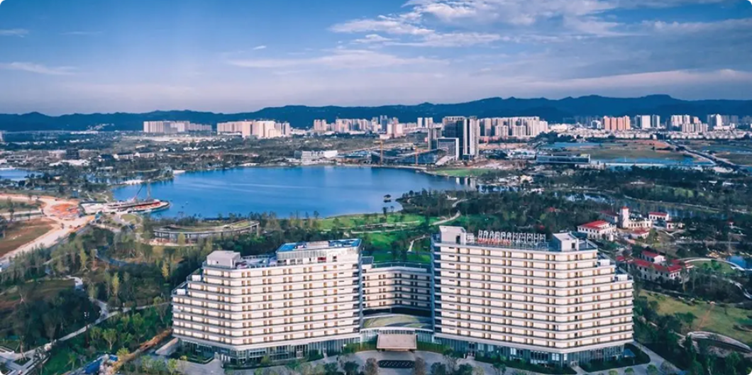 Aerial view of lakeside medical campus with city skyline and mountains in the background.