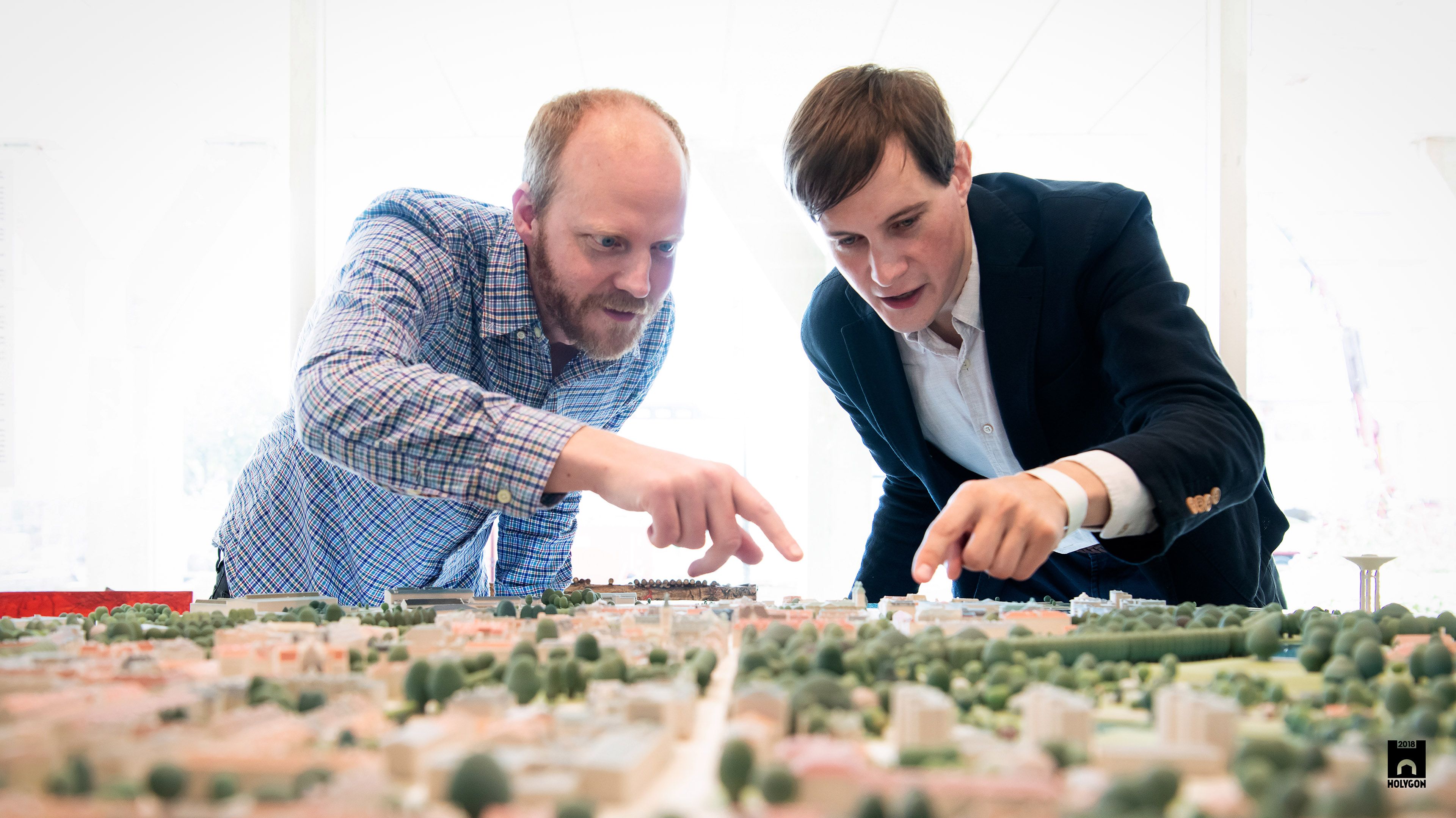 Two men examining a detailed city model, pointing at different buildings and landscapes.