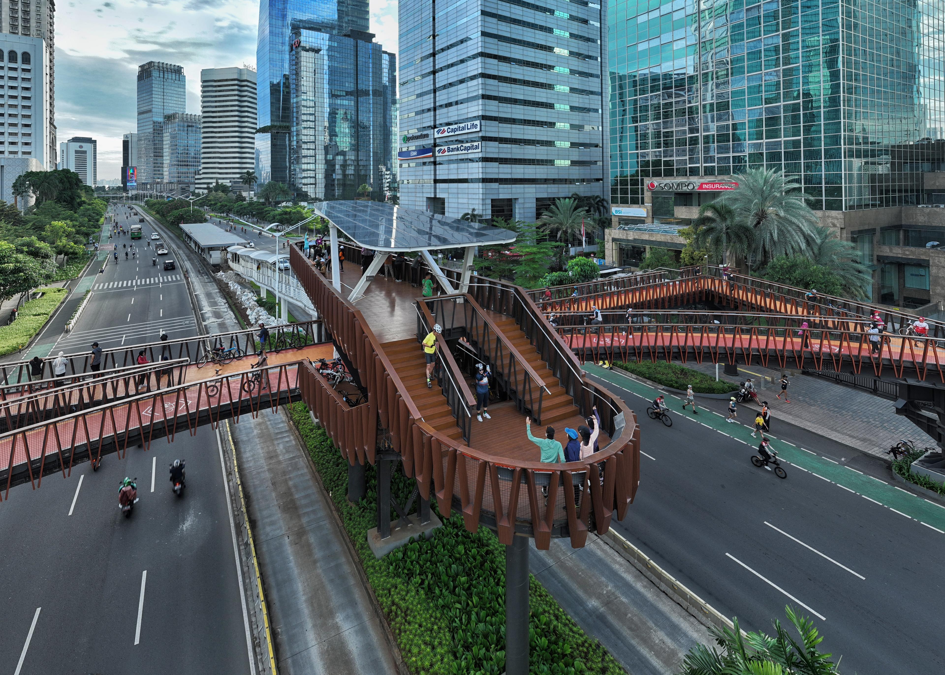The Pinisi Crossing Bridge in daylight above the city traffic and high-rise buildings in the background.