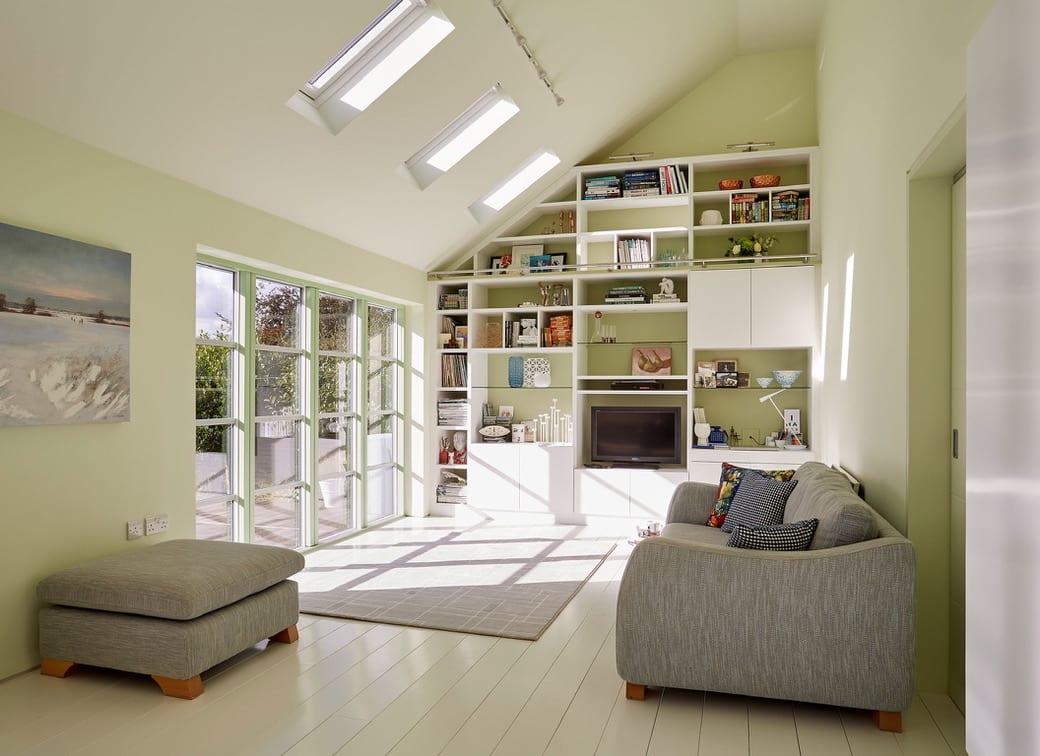 a custom-designed living room/study with a wall of windows, light green walls, and white built-in shelving